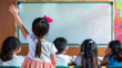 © evgenia_lo - Young Asian girl raising her hand eagerly in a classroom, surrounded by peers.