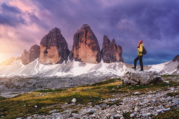 Wall Mural - girl with backpack on the stone and high mountain peaks at colorful sunset in autumn. tre cime, dolo