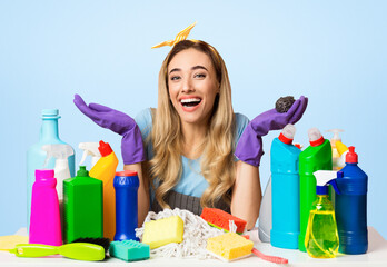 Smiling housewife in gloves and apron with cleaning supplies and brushes, isolated on pink background