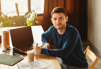 Poster - Positive Man At Laptop Computer Working Taking Notes Looking At Camera Sitting Indoor. Office Job.