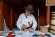 © Vasya - Romania, Suceava, September 21, 2024. A craftsman in traditional attire carefully carves a wooden spoon at his stall, showcasing his artisan skills and dedication to craftsmanship.