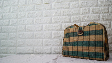 Stylish woven handbag with a checkered pattern in green and beige against a textured white brick wall. Ideal for eco-friendly fashion and rustic decor themes.