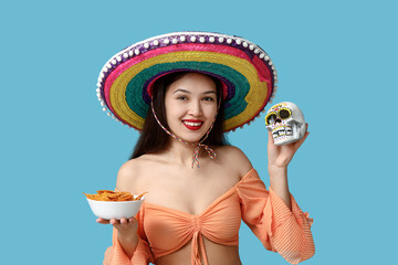 Wall Mural - Portrait of young woman with sombrero, painted human skull and tortilla chips on blue background. National Tortilla Chip Day celebration