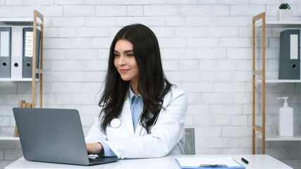 Poster - A young woman doctor sits at a clean, organized desk, focused on her laptop. The bright, minimalistic office features white brick walls and neat storage solutions.