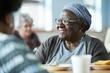 © CozyNessAI - An elderly woman sitting at a cafeteria table, looking content while enjoying a conversation. Old care home.
