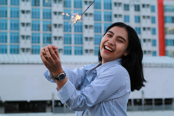 happy asian young woman holding sparklers to celebrate new year eve standing in outdoor roof top with city building background