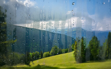 Poster - A view of rolling hills and a mountain range is seen through a window covered in raindrops.