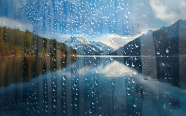 Poster - A view of a snow-capped mountain range reflected in a still lake through a rain-streaked window.