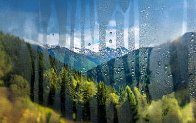Poster - A view of a mountain range covered in snow through a window with condensation.