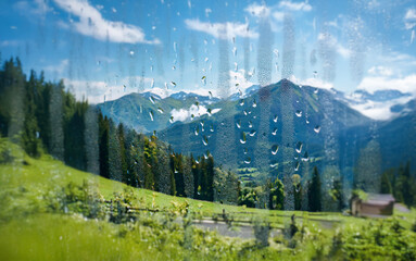 Poster - A view of a mountain range, a forest, a green field, a small house, and a pond, seen through a rain-streaked window.