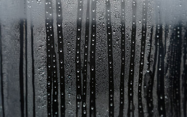 Poster - Raindrops cascade down a window pane, creating a blurred and abstract background.