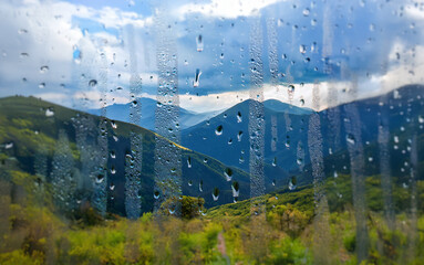 Poster - A view of rolling green hills through a window covered in raindrops.