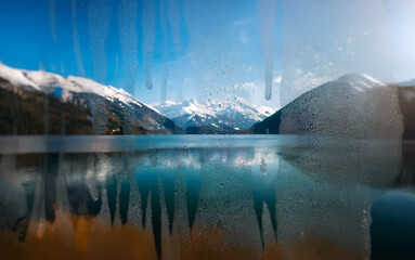 Poster - A view of a snow-capped mountain range reflected in a lake through a window covered in condensation.