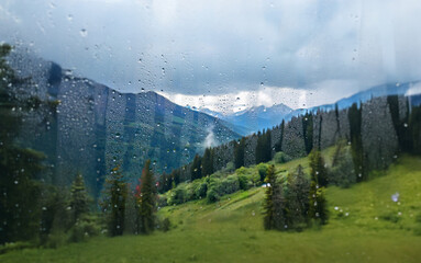 Poster - A view of a mountainous landscape through a window with raindrops.