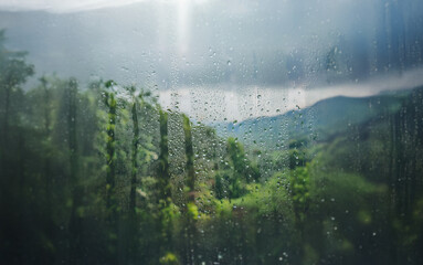 Poster - Rain falls on a window with a view of a forest and mountains in the distance.