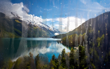 Poster - A view of a lake and mountains through a window covered in raindrops.