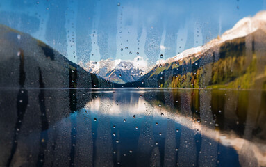 Poster - A view of a snow-capped mountain reflected in a lake through a rain-streaked window.