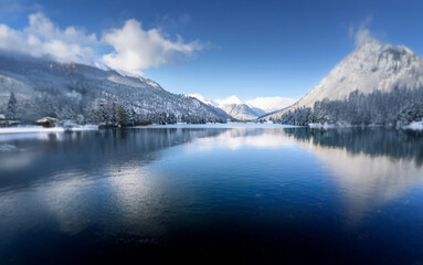 Poster - A serene winter landscape featuring a still lake reflecting a snowy mountain range and a clear blue sky.