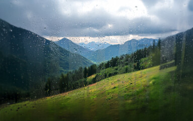 Poster - A view of green hills and mountains through a rain-streaked window.