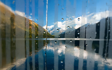 Poster - A view of snow-capped mountains and a blue lake through a rain-streaked window.