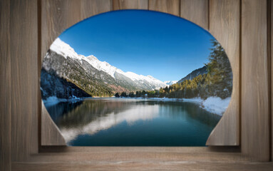 Poster - A scenic mountain lake with snow-capped peaks reflected in the calm water, seen through a rounded wooden window.