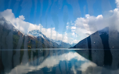 Poster - A view of a mountain range reflected in a still lake, with a cloudy sky above.