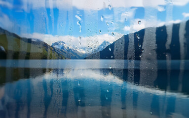 Poster - A view of a mountain range with a lake in the foreground is seen through a window with rain drops on it.