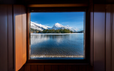 Poster - A view of a snow-capped mountain range reflected in a still lake, seen through a wooden window.