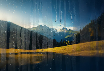 Poster - A mountain range viewed through a rain-streaked window, with the sun shining through the clouds.