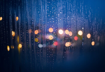 Aufkleber - Rain falls on a window pane, creating a blurry view of city lights.