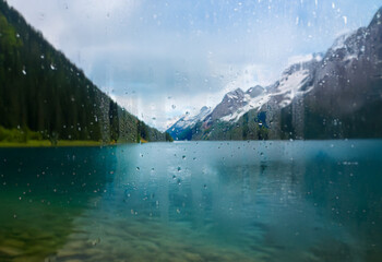 Aufkleber - A view of a serene lake surrounded by mountains through a rain-streaked window.