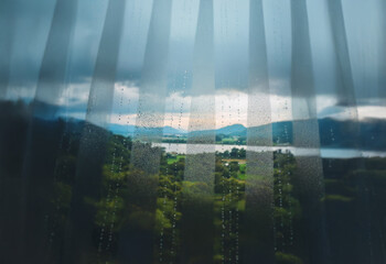 Poster - A view of a lake and mountains through a sheer curtain with raindrops.