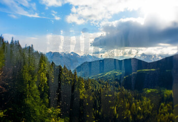 Poster - A scenic view of rolling green hills with snow-capped mountains in the distance,  a hint of blue sky peeks through the clouds.