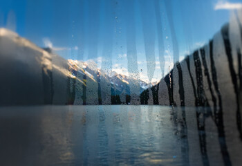 Poster - A blurry view of a snow-capped mountain range through a rain-streaked window.