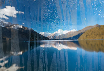 Poster - A view of a lake and mountains seen through a window covered in raindrops.