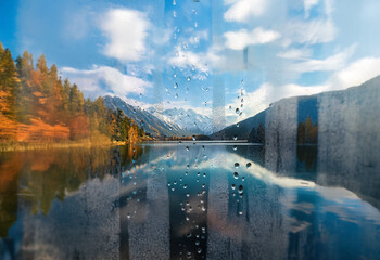 Poster - A picturesque view of a mountain lake through a rain-streaked window with a reflection of the surrounding scenery.