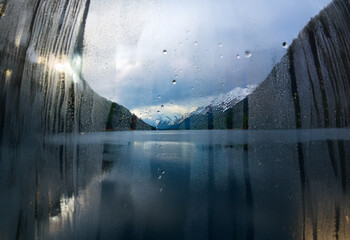 Poster - A scenic mountain lake is viewed through a window with raindrops clinging to the glass.