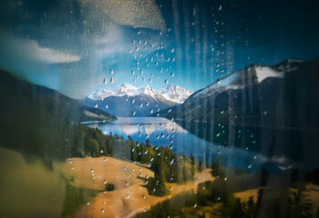 Poster - A view of a mountain lake and snow-capped peaks through a rain-streaked window.