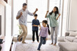 © fizkes - Couple of cheerful Indian parents and two active sibling kids dancing to music on carpet in living room, enjoying songs, activity, funny family party, leisure, smiling, laughing. Full length shot