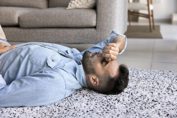 Tired depressed Hispanic man lying on home floor, keeping hand on closed eyes, feeling exhausted, caring for back relaxation, sleeping, thinking on financial problems, emotional crisis, fatigue