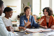 © Mediaphotos - Teacher interacting with diverse group of engaged students during study session around table, with books and educational materials in background, creating a collaborative learning atmosphere