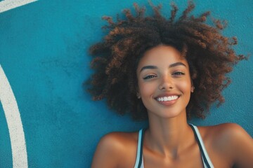 Poster - A smiling woman with curly hair standing in front of a blue wall, a simple and cheerful moment