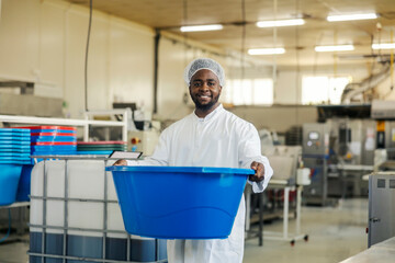 Portrait of smiling diverse food industry worker with plastic container in hands looking at camera.