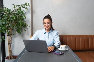 One young businesswoman sitting in cafeteria taking a coffee break while working online on laptop computer. Business female professional occupation e-commerce and remotely finance and economy research