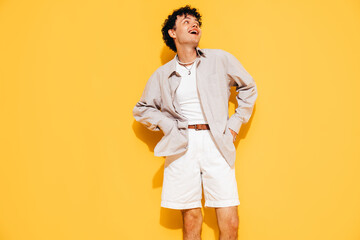 Young attractive man with short curly hair hairstyle. Smiling handsome male in casual stylish shirt and shorts clothes posing in studio, isolated on yellow. Cheerful and happy model