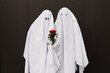 © VISTA by Westend61 - Young couple wearing ghost costumes and standing with flowers in front of wall