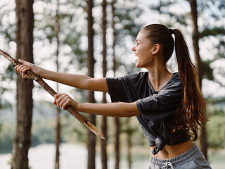 Joyful young woman playing with a stick in a forest, enjoying nature and the outdoors, showcasing freedom and happiness Natural setting with trees in the background