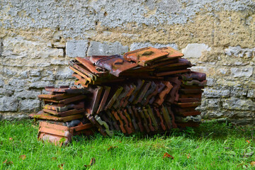 Stack of orange roof tiles in green grass against stone wall