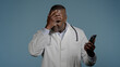 © Yuliia - Upset frustrated african american man doctor reading bad medical news on mobile phone in blue background receive notification worried male healthcare worker stressed over broken smartphone low battery