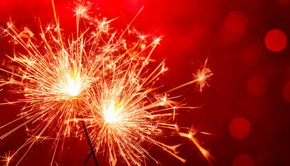 Two lit sparklers on a red background with highlights.